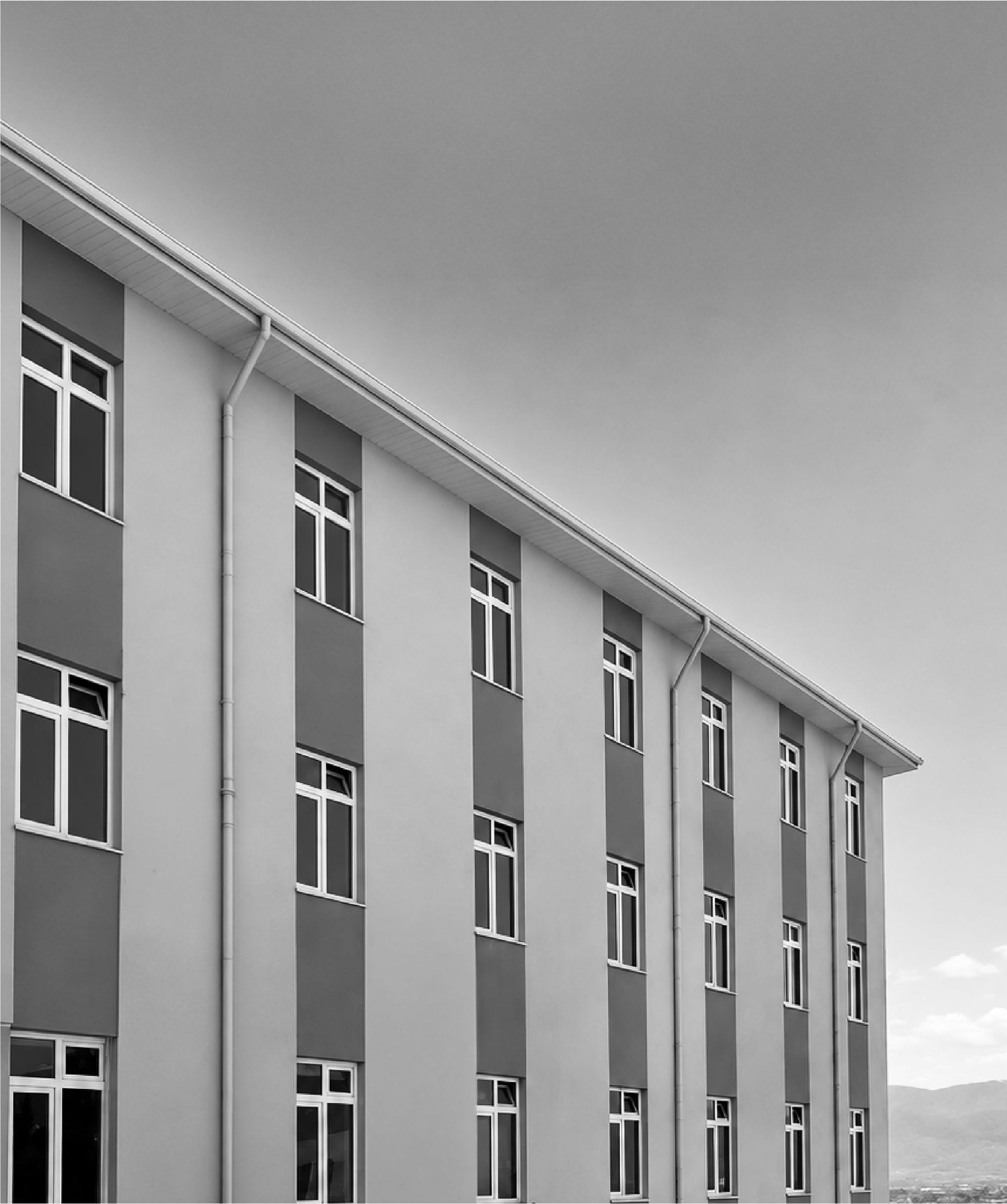 Düzce Halk Sağlığı Laboratuvarı binası, siyah beyaz: üç katlı yapının köşeden görünümü, arkasında bulutlu gökyüzü.